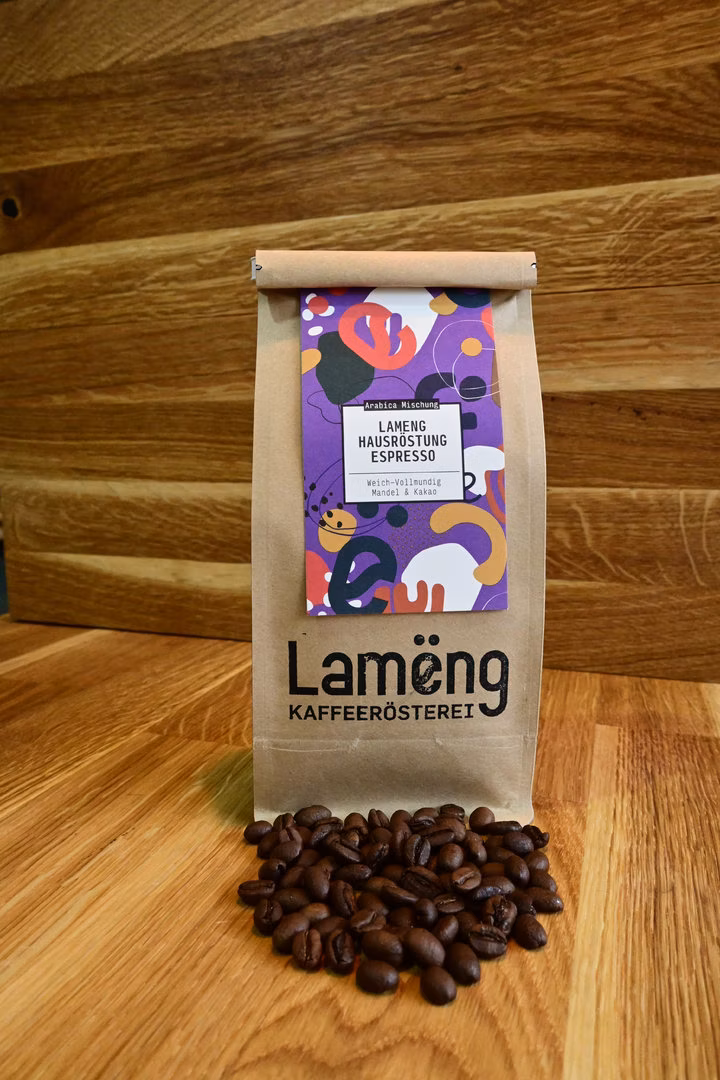 Lamëng-Kraftpapier-Tüte mit Hausröstung-Etikett, davor frisch geröstete Espresso-Bohnen auf Holzboden