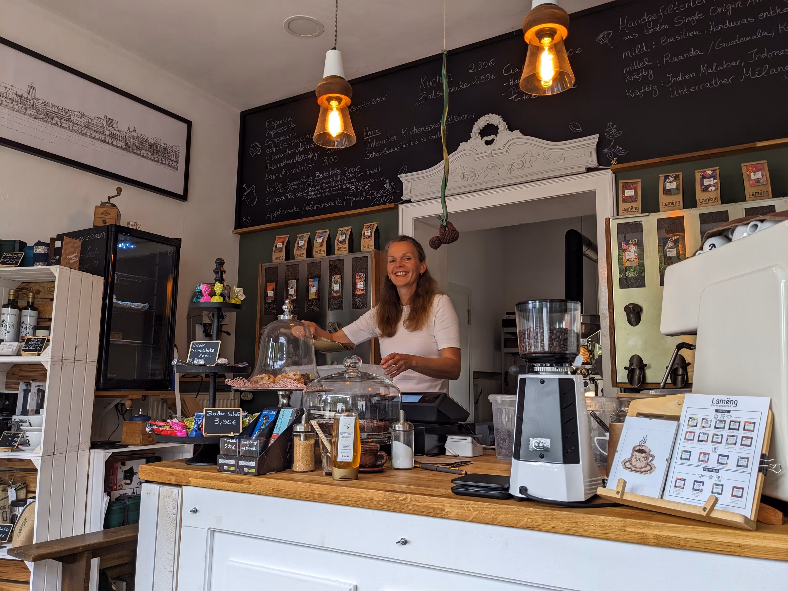 Annika hinter der Lamëng-Café-Theke in Düsseldorf-Unterrath, dahinter Tafel-Menüs mit Tagesangeboten und Vintage-Pendelleuchten