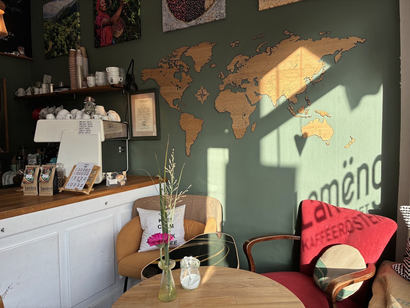 Lamëng-Espressotasse mit dem ë-Logo, daneben eine kleine Vase mit Tulpe und Anemone, Macarons im Hintergrund auf hölzerner Café-Theke